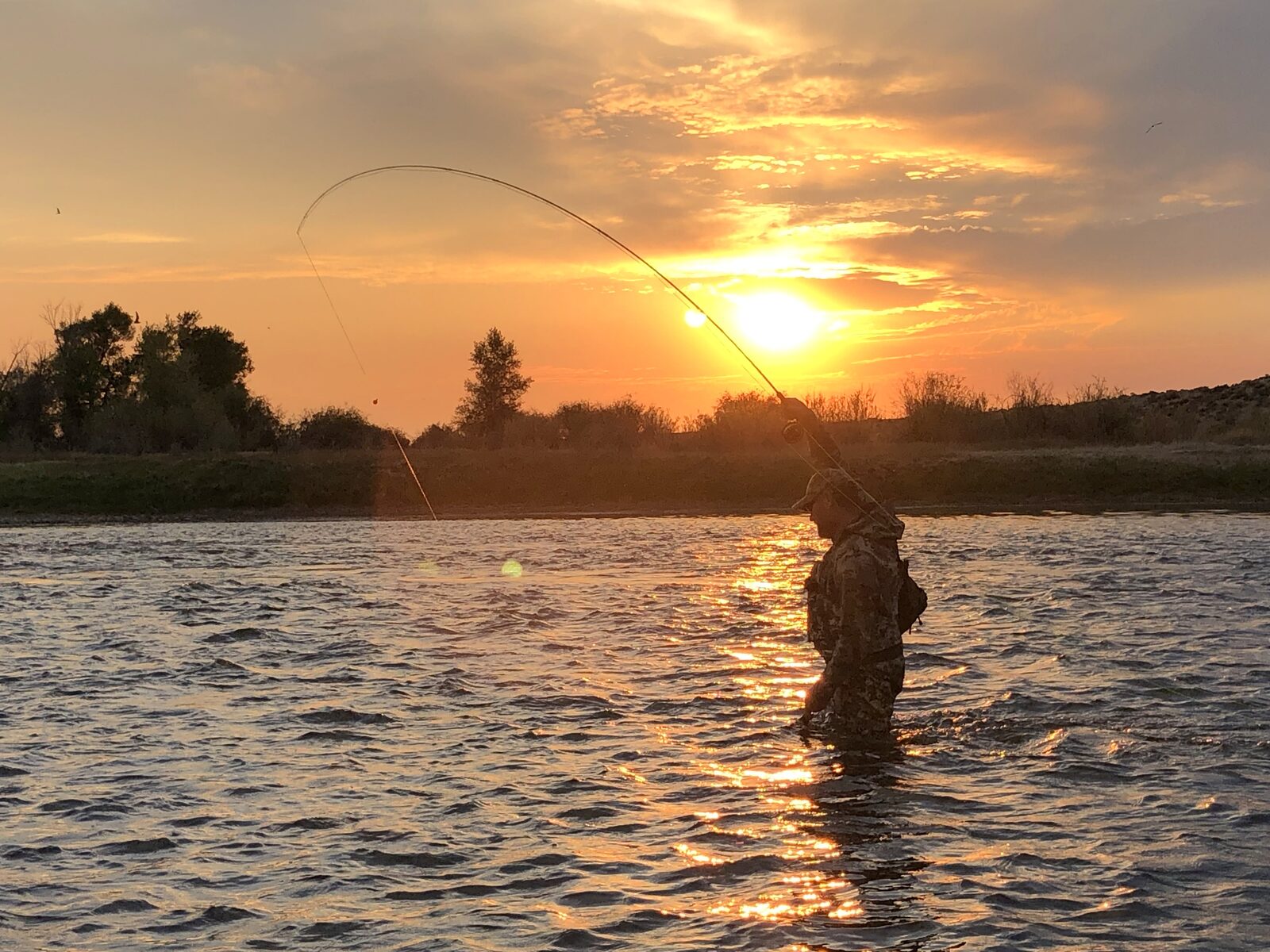 Angler wading and casting a fly rod at sunset on a mountain river