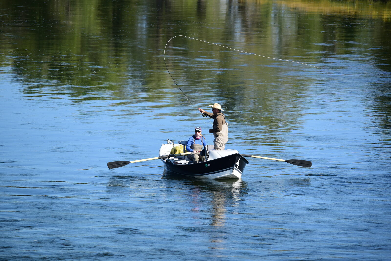 Angler casting a fly line from a drift boat on calm water