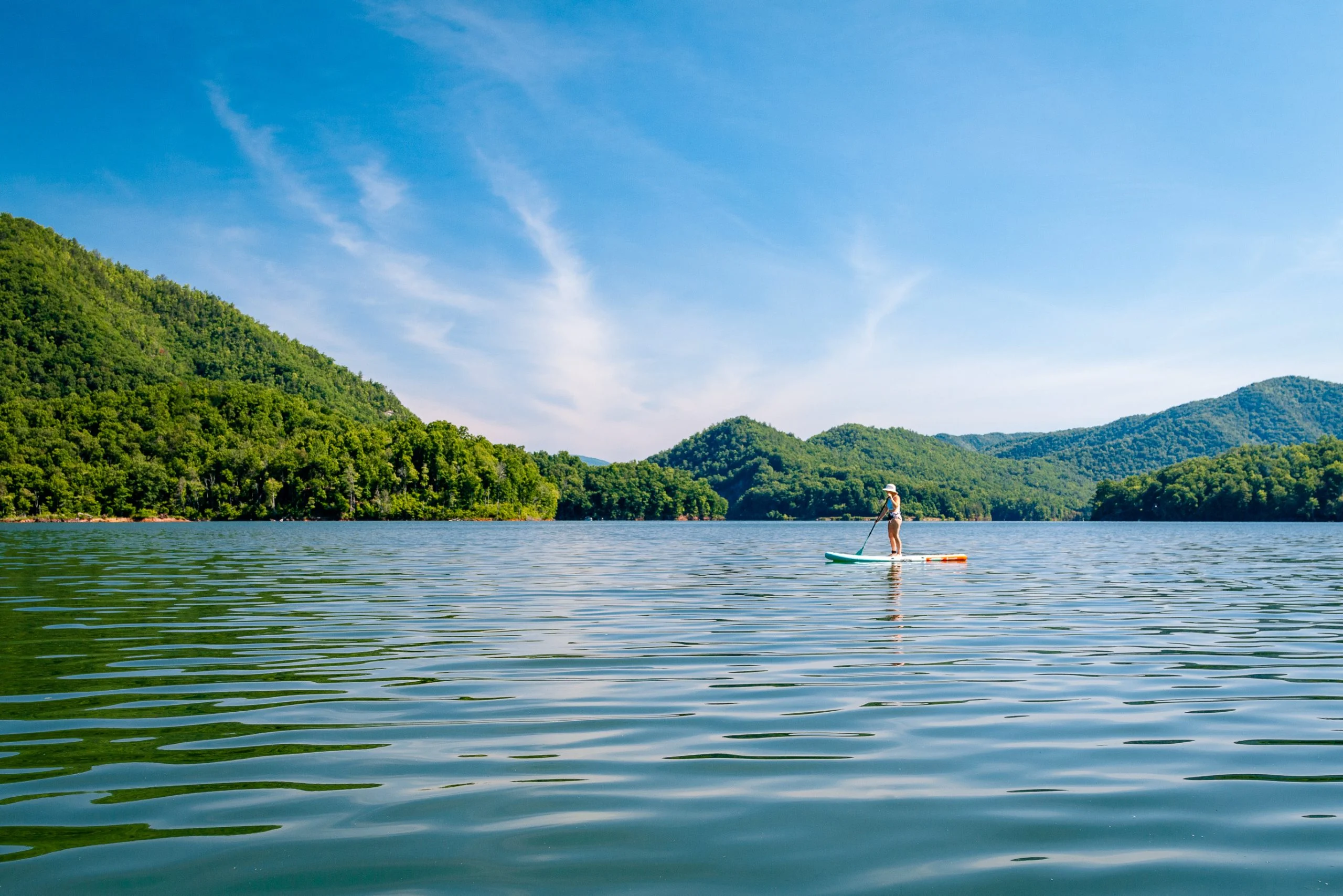 Paddleboarder on a calm mountain lake under blue sky