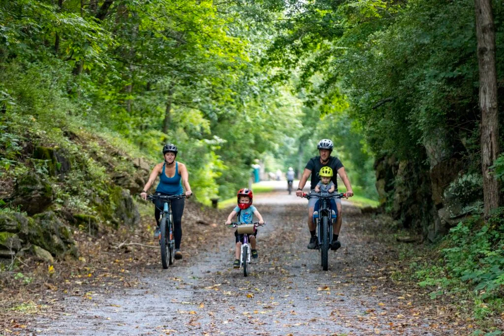 Family of four biking the Tweetsie Trail under a green canopy