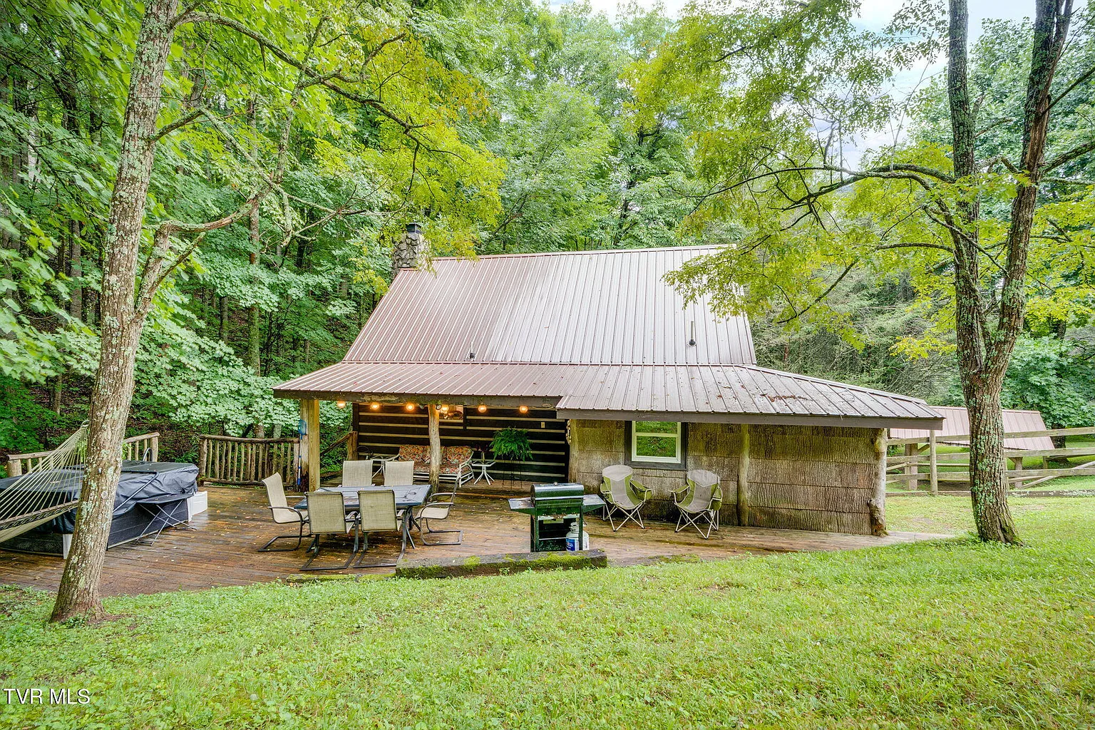 Log cabin at Misty Hollow with covered deck, outdoor dining, grill, and hot tub under hardwood trees